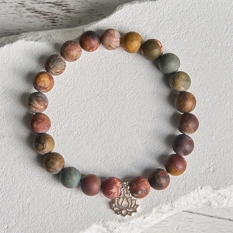 Picasso Jasper Lotus Bracelet – flat lay on weathered white stone, matte earthy beads with lotus pendant