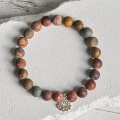 Picasso Jasper Lotus Bracelet – flat lay on weathered white stone, matte earthy beads with lotus pendant
