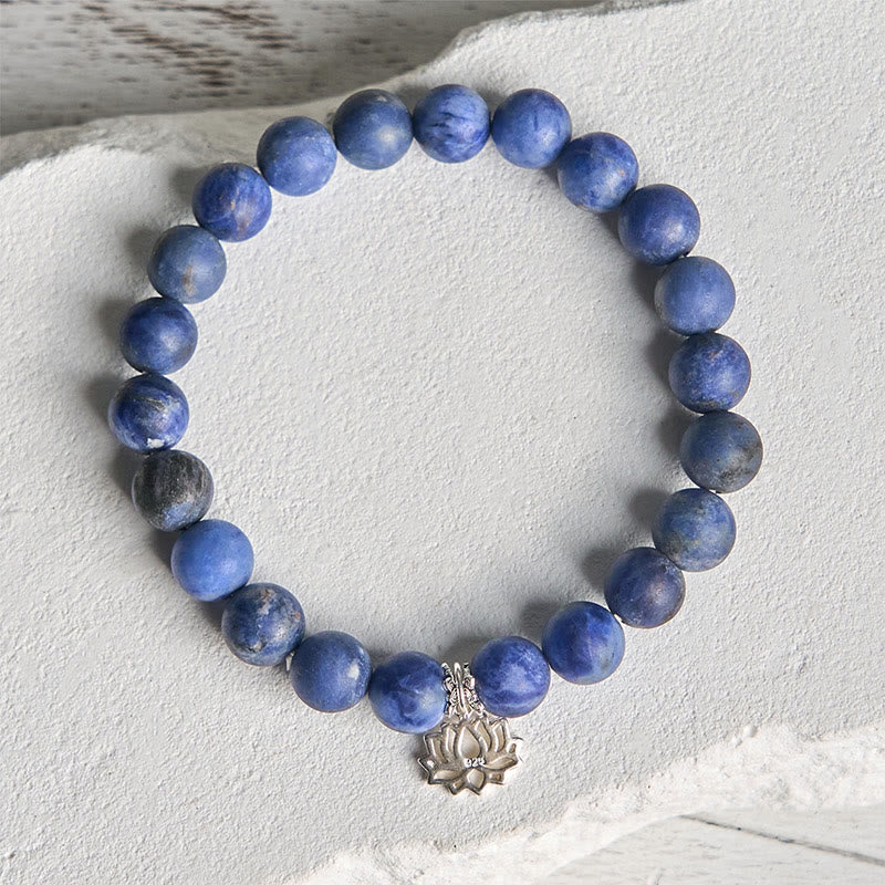 Sodalite Lotus Bracelet – overhead flat lay on white stone surface, matte blue beads and lotus charm detail