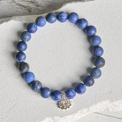 Sodalite Lotus Bracelet – overhead flat lay on white stone surface, matte blue beads and lotus charm detail