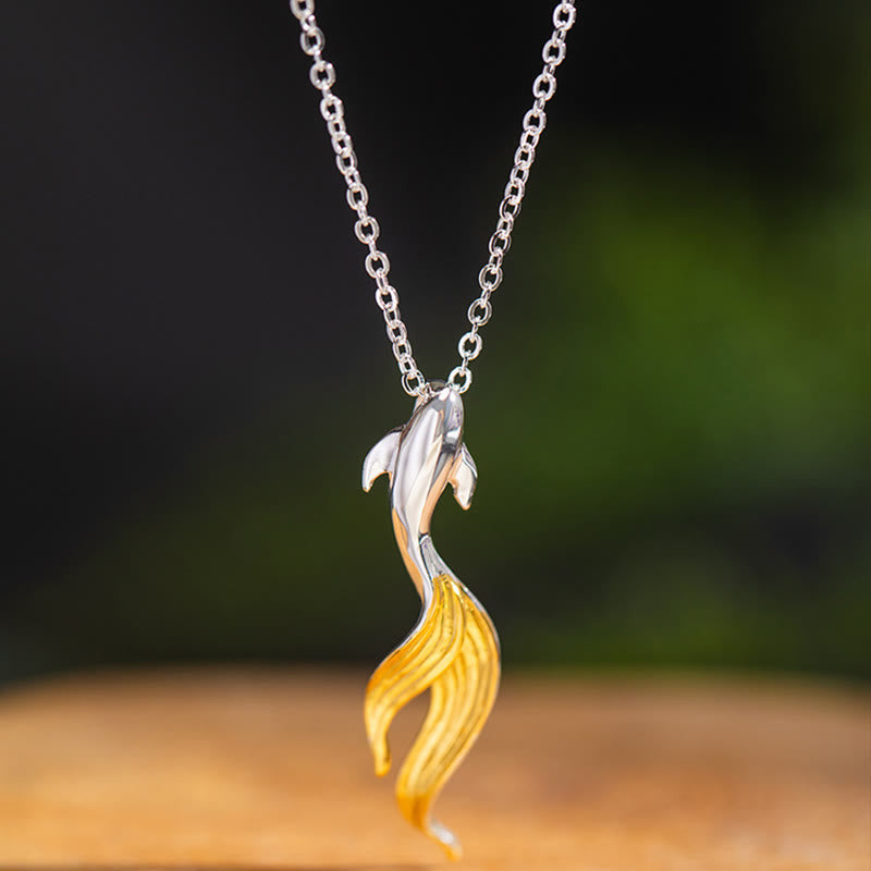 Silver Golden Koi Fish Luck Necklace – upward-swimming koi with gold tail on wooden surface, dark foliage bg
