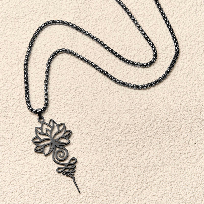Lotus Unalome Necklace – Black lotus-unalome pendant on chain flat-laid on textured cream, enlightenment pendant