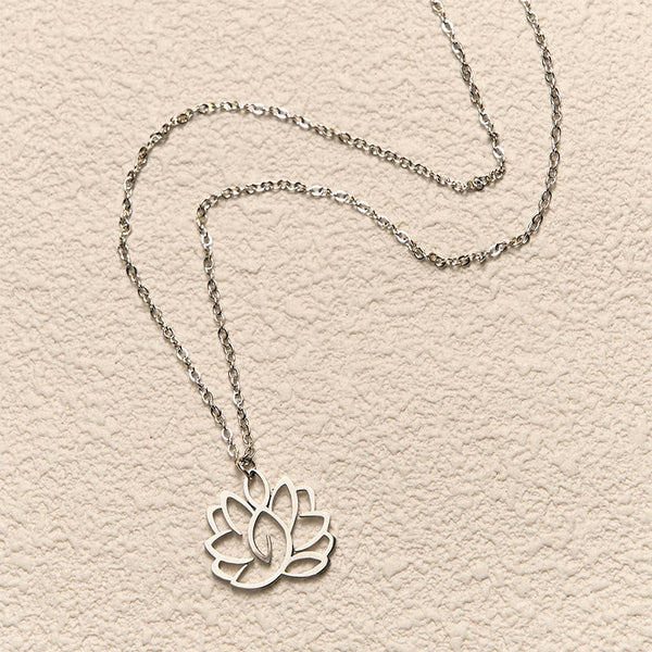 Hollow Lotus Necklace – Silver cutout lotus pendant flat-laid on cream textured background, purity pendant