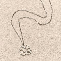 Hollow Lotus Necklace – Silver cutout lotus pendant flat-laid on cream textured background, purity pendant