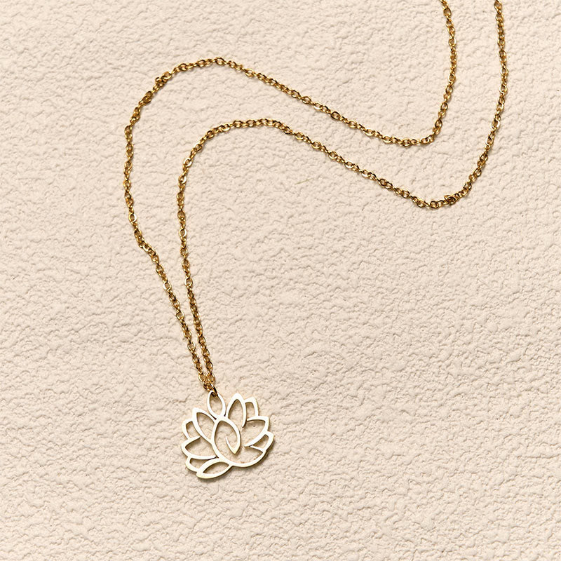 Hollow Lotus Necklace – Gold cutout lotus pendant flat-laid on textured cream, spiritual purity jewelry
