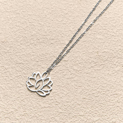 Hollow Lotus Necklace – Silver openwork lotus pendant on textured cream at angled view, enlightenment symbol