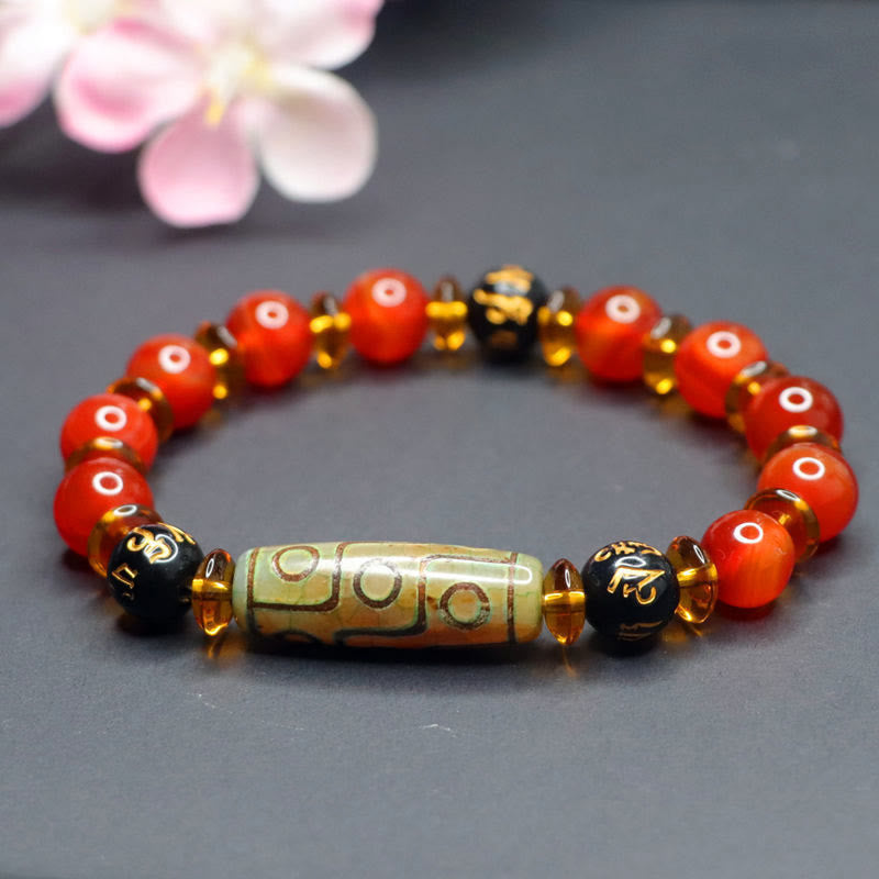 Red Agate Nine-Eye Dzi Bead Bracelet – slightly elevated angle, warm carnelian eye beads against dark gray with pink bloom