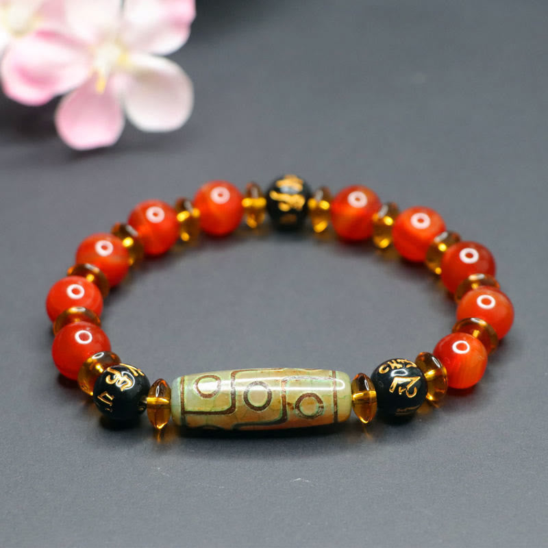 Red Agate Nine-Eye Dzi Bead Bracelet – circular arrangement with greenish dzi barrel bead and gold mantra accents, bokeh