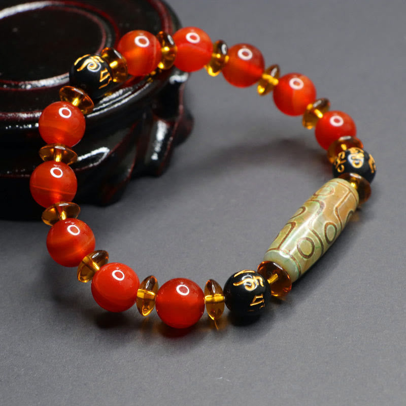 Red Agate Nine-Eye Dzi Bead Bracelet – draped on carved dark wood stand, amber spacer sparkle and dzibead eye patterns