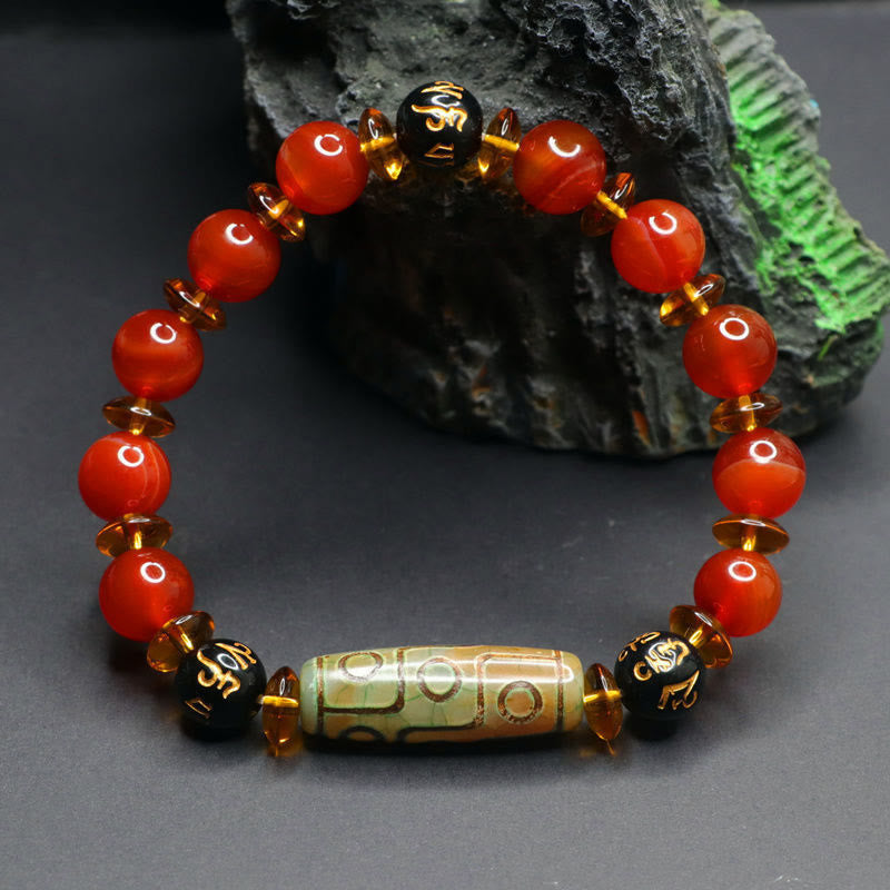 Red Agate Nine-Eye Dzi Bead Bracelet – dark stone prop backdrop highlighting polished red beads and gold Tibetan inscriptions