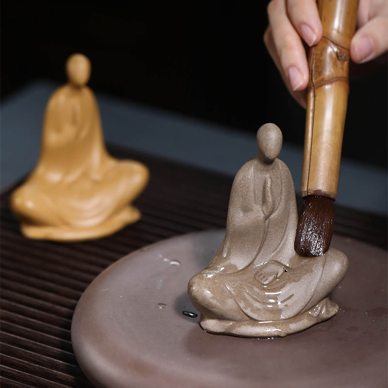 Ceramic Formless Buddha Prayer Statue – bamboo brush touching gray figure, tea ritual scene, tan statue in soft background