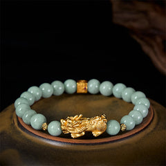 Golden Pi Xiu Charm Jade Prosperity Beaded Bracelet – Green jade bracelet with gold Pi Xiu on ceramic plate, side view