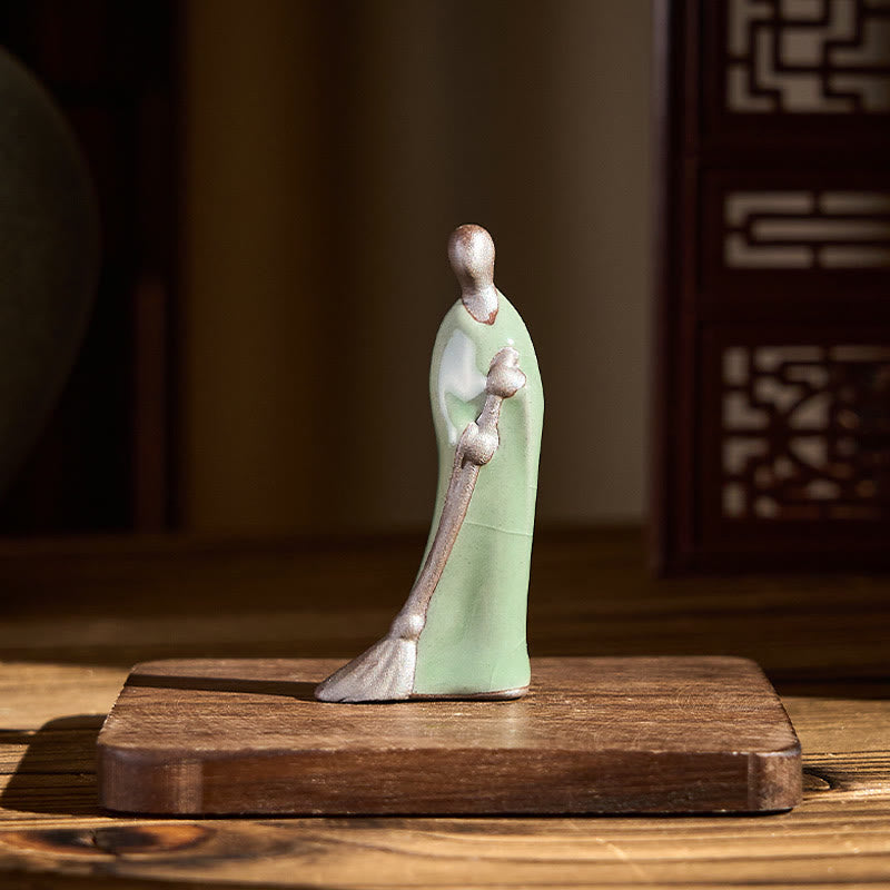 Ceramic Sweeping Monk Buddha Statue – monk on wood base in warm room, natural light decor