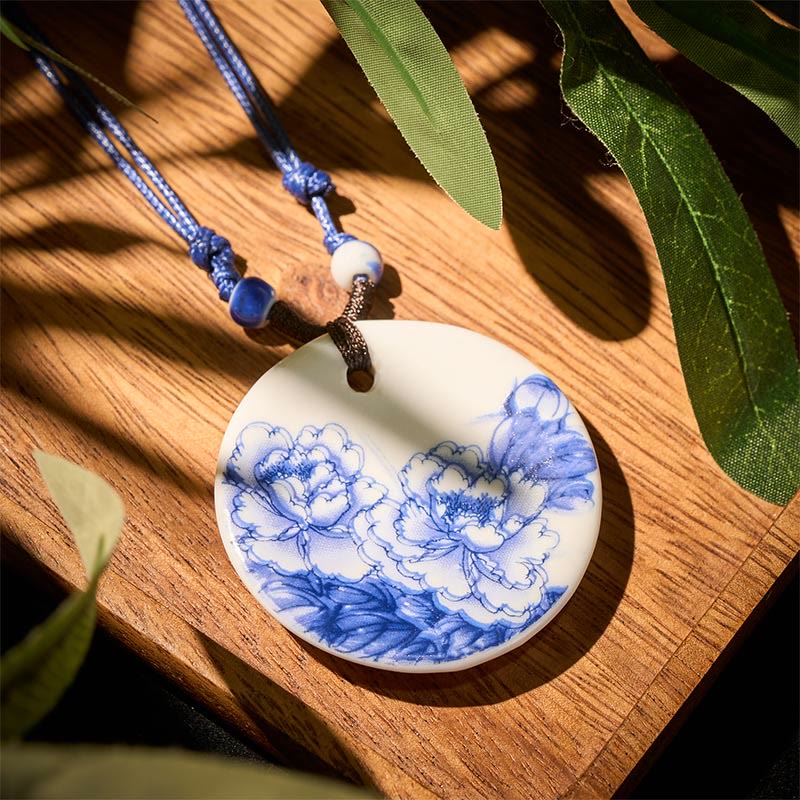 Ceramic Peony & Lotus Pendant – Two peony blooms on white ceramic over wood grain, blue cord necklace
