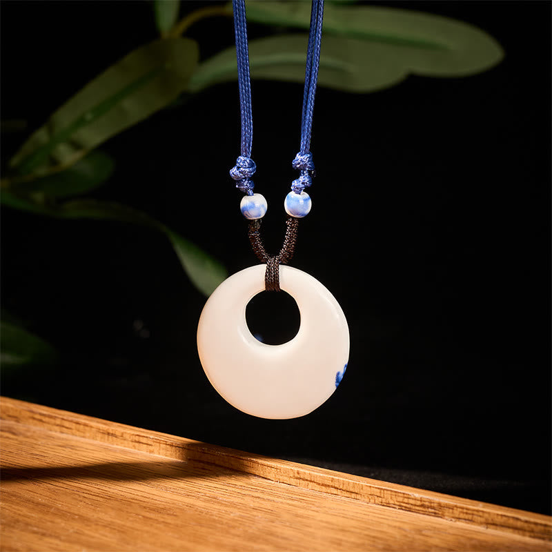Ceramic Peony & Lotus Pendant – Cream porcelain disc with subtle blue edge in dark studio, ceramic necklace