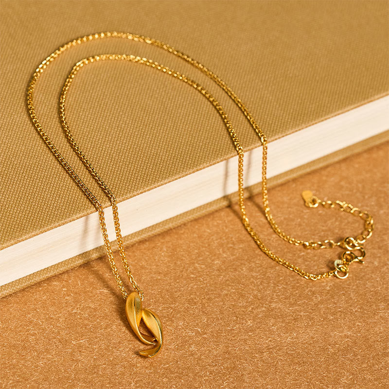Double Koi Fish Gold Necklace Pendant – gold pendant draped on book with kraft paper, wealth talisman necklace