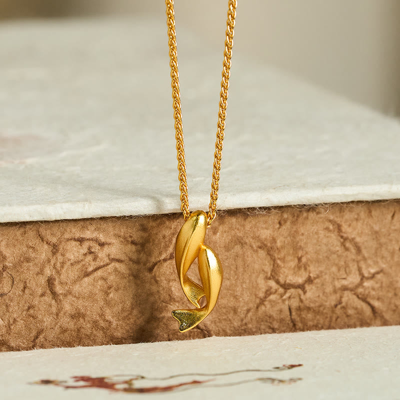 Double Koi Fish Gold Necklace Pendant – gold pendant on crackled brown texture low angle, wealth jewelry