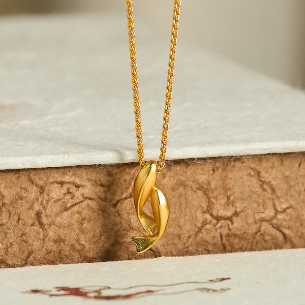 Double Koi Fish Gold Necklace Pendant – gold pendant on crackled brown texture low angle, wealth jewelry