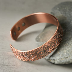 Tree of Life Copper Cuff Bracelet – leaning on gray stone highlighting embossed tree design, womens cuff