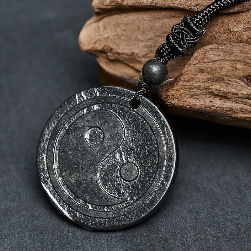 Natural Shungite Carved Yin Yang Pendant - side angle on stone surface, shungite talisman