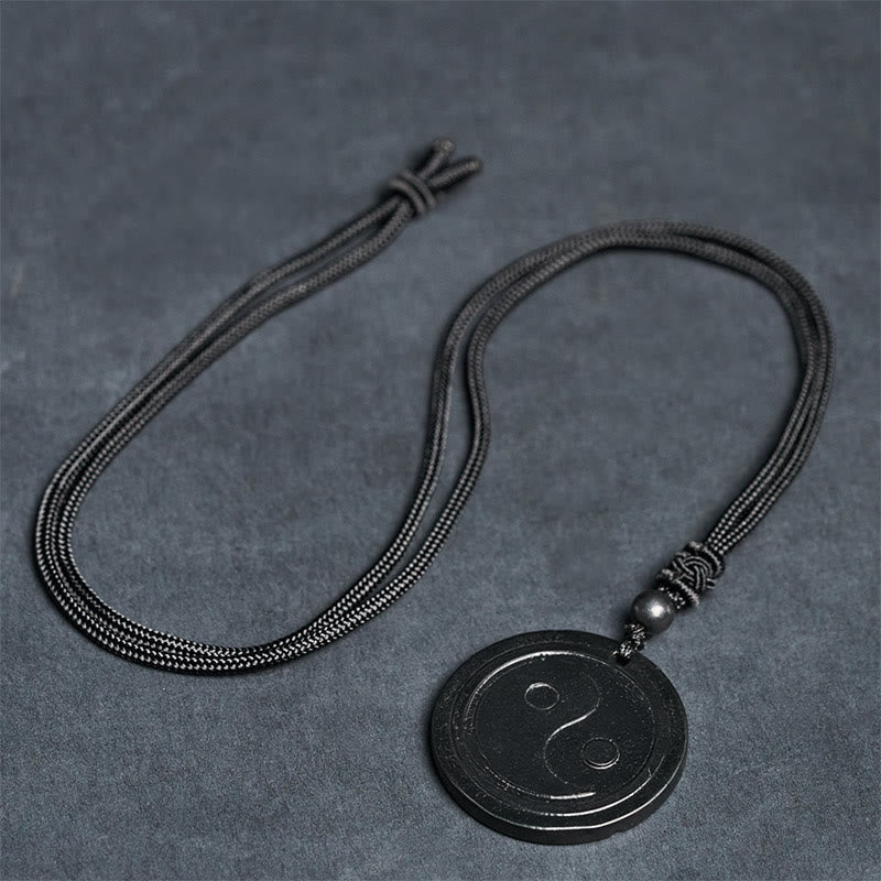 Natural Shungite Carved Yin Yang Pendant - flat lay on gray surface, shungite necklace