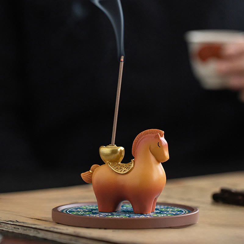 Year of Horse Ingot Incense Burner – Terracotta horse with gold saddlebag on patterned base, lit incense, teacup background, incense burner