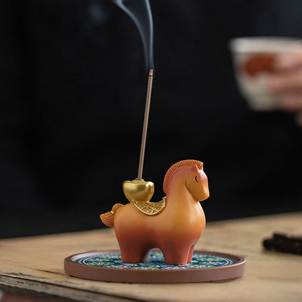 Year of Horse Ingot Incense Burner – Terracotta horse with gold saddlebag on patterned base, lit incense, teacup background, incense burner