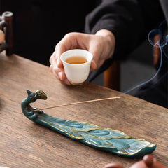 Peacock Shape Ceramic Incense Burner – Teal peacock incense burner with gold feather details, lit stick with smoke, teacup in background, ceramic incense holder