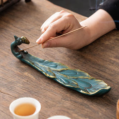Peacock Shape Ceramic Incense Burner – Hand placing incense into teal and gold peacock burner on wooden table, ceramic incense holder
