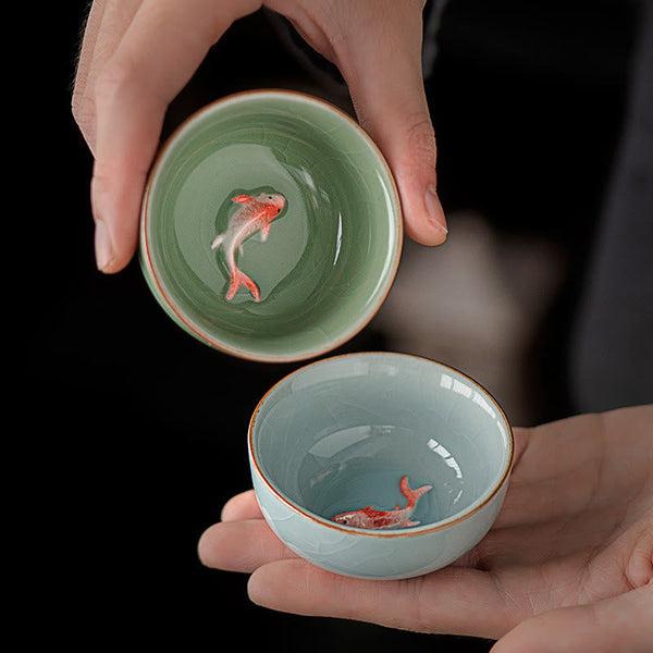 Hand Painted Koi Fish Ceramic Teacup – two celadon cups in hands with koi visible, hand painted tea set