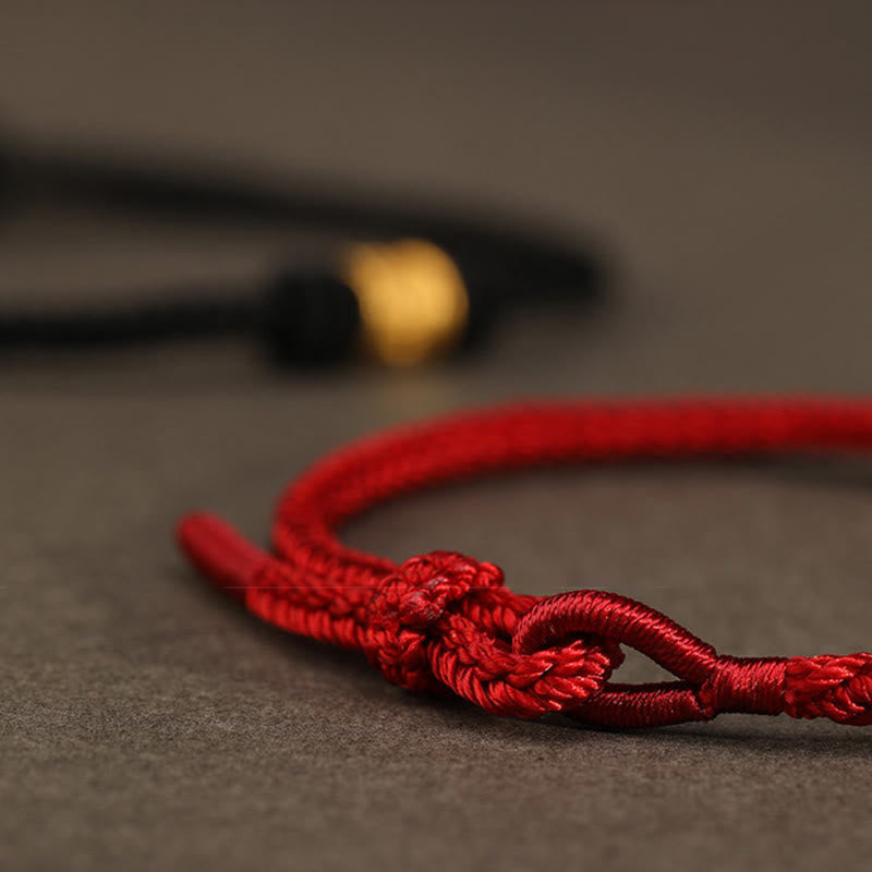 999 Gold Om Mani Padme Hum Red String Bracelet – close-up of red cord knot detail with gold bead in bokeh background, red cord jewelry