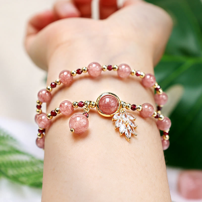 Strawberry quartz double-wrap bracelet worn on wrist against green botanical background with pink gemstone beads gold accents and crystal leaf spray charm