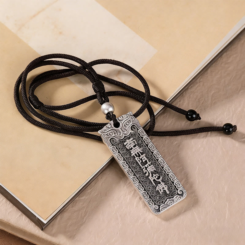 Namo Amitabha Copper Rope Necklace - Engraved pendant resting on book with fabric backdrop, Zen jewelry