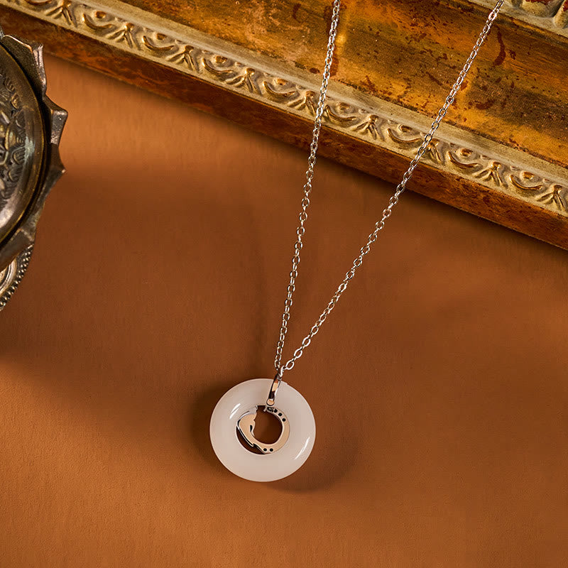 Koi Fish Peace Buckle Necklace – 45-degree view on caramel surface, jade disc with silver crescent, gilded frame