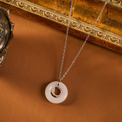 Koi Fish Peace Buckle Necklace – 45-degree view on caramel surface, jade disc with silver crescent, gilded frame