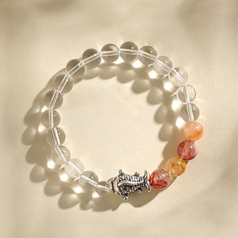Clear Quartz Koi Fish Bracelet – top-down on cream linen, clear beads with warm stones, koi charm, caustic light