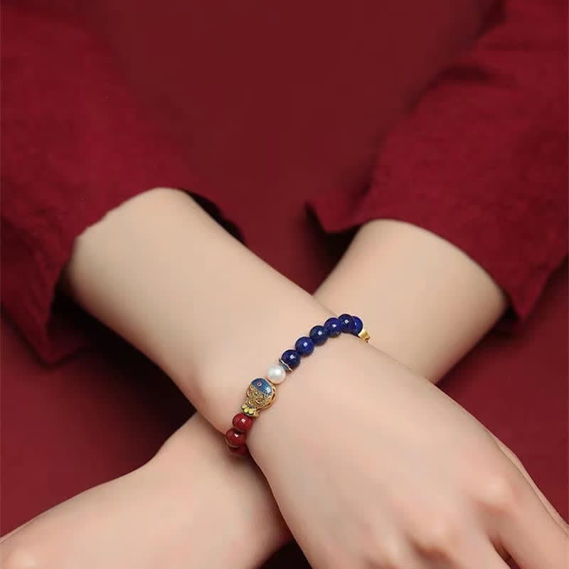 Cinnabar Lapis Lazuli Koi Fish Bracelet – worn on crossed wrists, close-up on burgundy fabric background