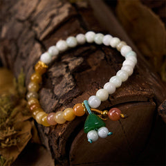 Multicolor jade bracelet with carved green lotus charm on dark wood, white yellow amber gradient beads
