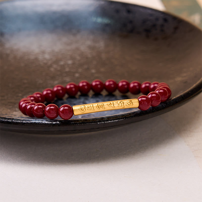 Cinnabar Om Mani Padme Hum Bracelet – Gold cylinder focal on dark ceramic dish, cinnabar bead bracelet