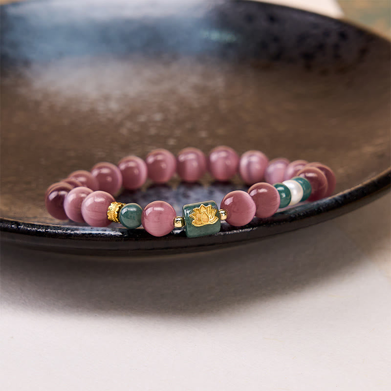 Purple Cat’s Eye Lotus Enlightenment Bracelet – Resting on dark ceramic dish, mauve cat’s eye beads with green jade lotus charm, mindful jewelry