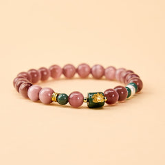 Purple Cat’s Eye Lotus Enlightenment Bracelet – Flat lay view showing mauve cat’s eye beads, gold lotus focal bead and green accents, gemstone bracelet