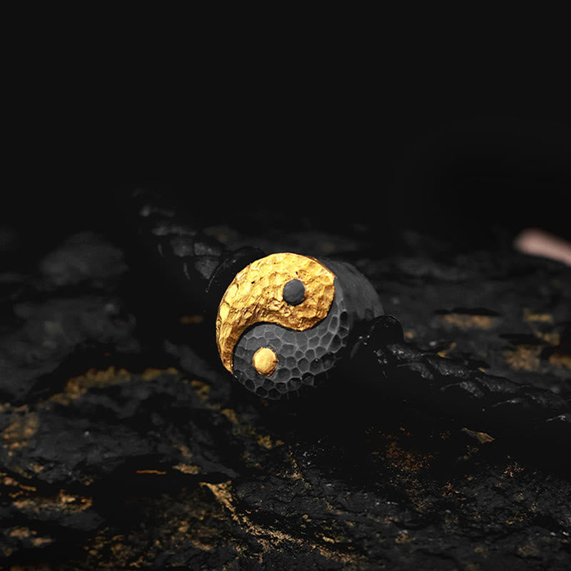 Yin Yang Bagua Leather Bracelet - Hammered gold yin yang bead close-up on dark volcanic rock, artisan jewelry