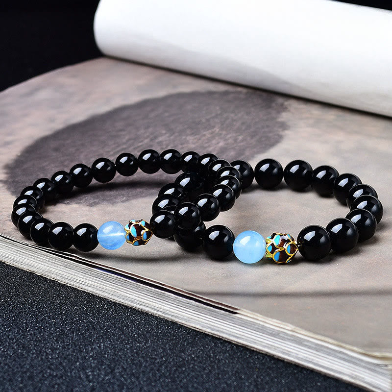 Black Obsidian Lotus Purification Bracelet - stacked pair on ink wash art book, lotus charm detail