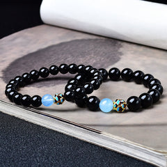 Black Obsidian Lotus Purification Bracelet - stacked pair on ink wash art book, lotus charm detail