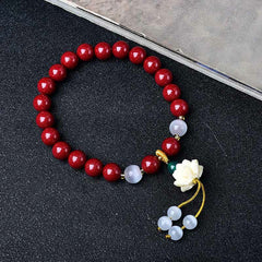 Cinnabar Cat's Eye Lotus Blessing Bracelet - top-down flat lay on black textured fabric, cinnabar bead bracelet