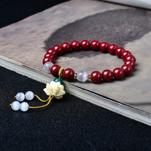 Cinnabar Cat's Eye Lotus Blessing Bracelet - 45-degree view on calligraphy book, lotus pendant and cord tassel
