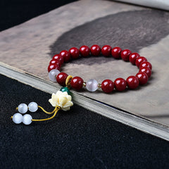 Cinnabar Cat's Eye Lotus Blessing Bracelet - 45-degree view on calligraphy book, lotus pendant and cord tassel