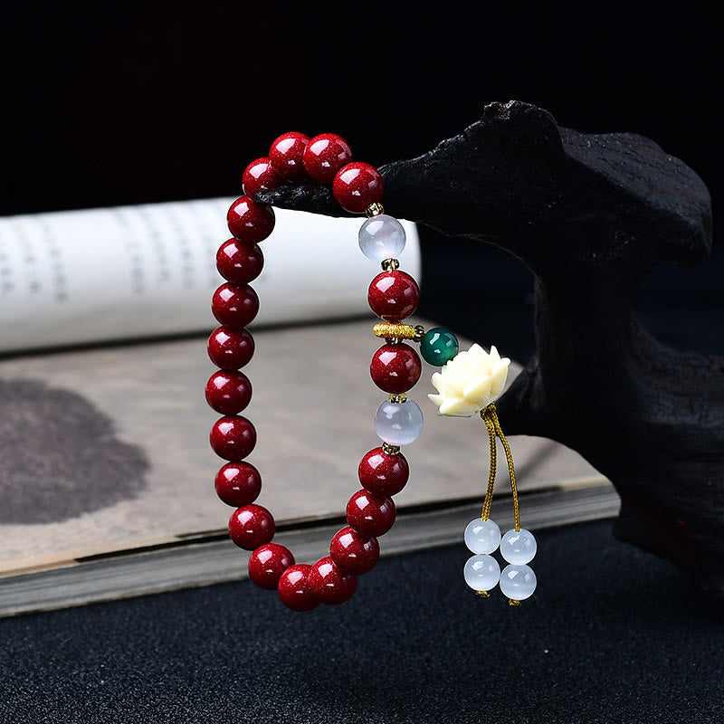 Cinnabar Cat's Eye Lotus Blessing Bracelet - draped on wooden stand with tassel detail, cinnabar red beads