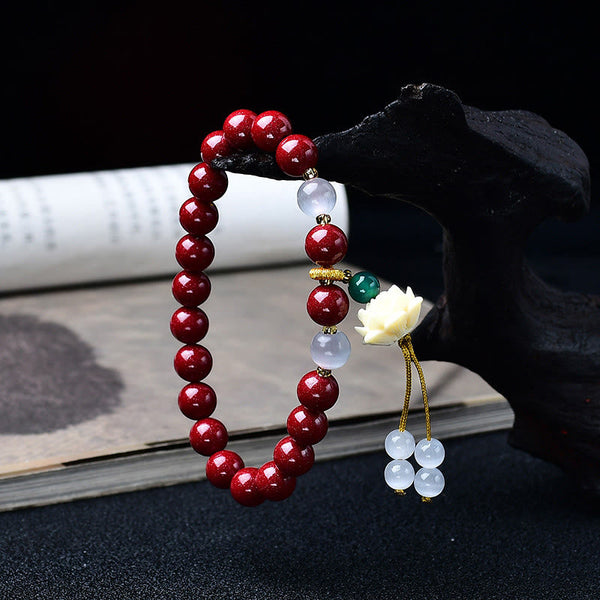 Cinnabar Cat's Eye Lotus Blessing Bracelet - draped on wooden stand with tassel detail, cinnabar red beads