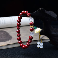 Cinnabar Cat's Eye Lotus Blessing Bracelet - draped on wooden stand with tassel detail, cinnabar red beads